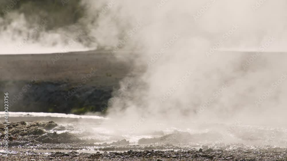 Hot boiling water splashes with water drops and hot thick steam swirling above. Natural physic science 4K cinematic hot geyser eruption on sunny summer day in Yellowstone National Park 4K footage.