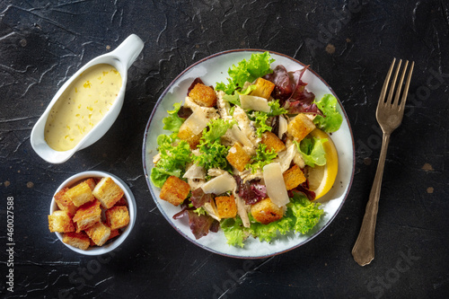 Chicken Caesar salad, overhead flat lay shot with the classic mayonnaise based sauce and croutons, on a black background