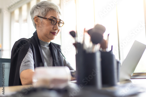 Senior female makeup artist learning online class on laptop computer at home office.