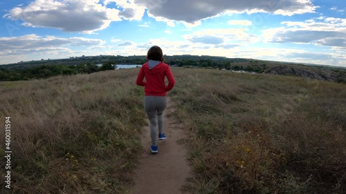 The woman runs along the path to the river. View from the back. Fitness concept.