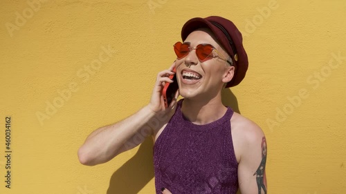 young gay man using smartphone and laughing with yellow background in sunny day photo