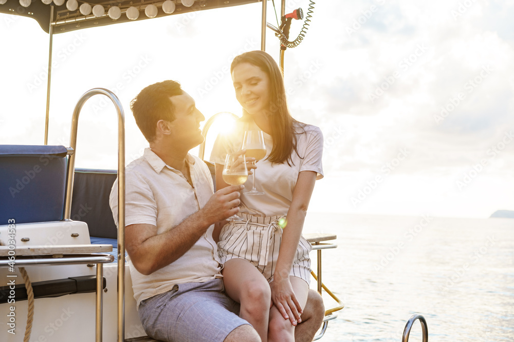Fototapeta premium Young loving couple sitting on the yacht deck and drinking wine