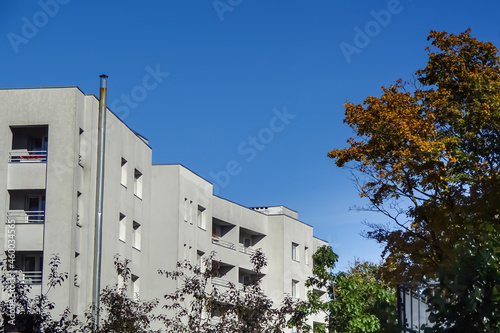 Close up of a grey house, building house with balconies and clear blue sky background. Green and autumn yellow tree foliage on the right. Kopli, Tallinn, Estonia. September 2021