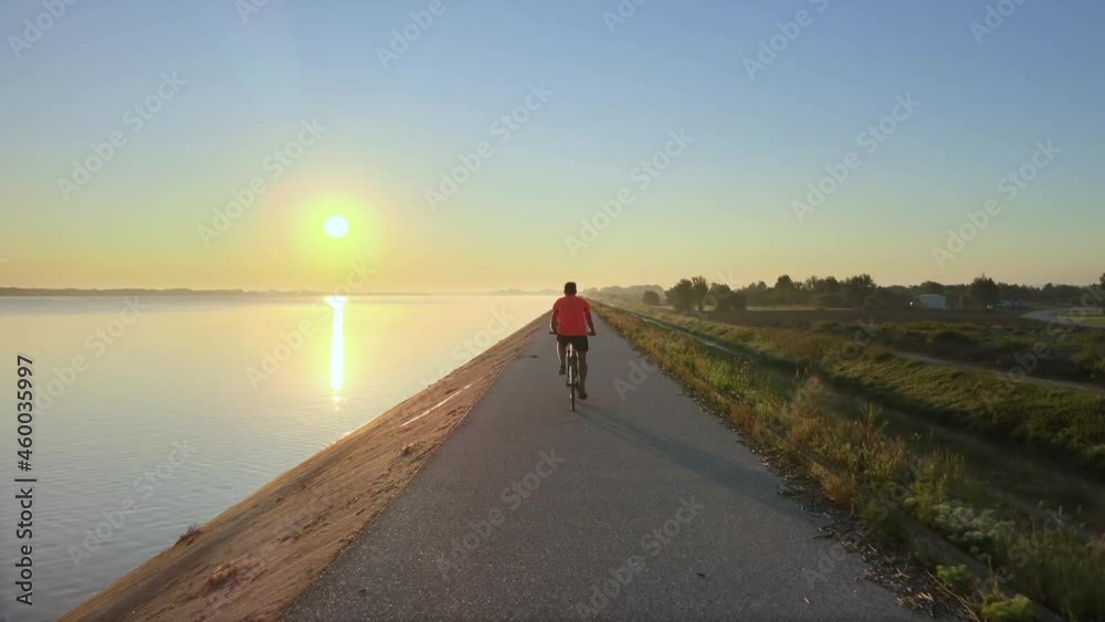 Man riding bike on riverside cycle path at sunset, 4K aerial rear follow shot Man riding bike on riverside cycle path at sunset, 4K aerial rear follow shot