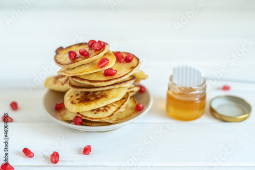 Miniature pancakes with fresh honey and pomegranate seeds for Jewish holiday Rosh Hashanah over white wooden background. photo