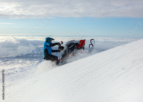 a snowmobiler rides and jumps in the snowy mountains. prof pilot of a mountain snowmobile in bright gear without brands for travel advertising