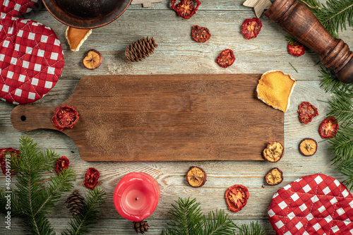 Brown cutting board on a wooden background. Around it are green coniferous branches, festive accessories. Concept of New Year, top view and copy space