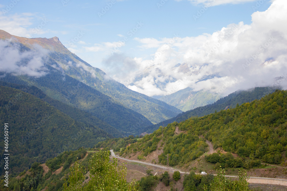 Summer mountain landscape in the Caucasus mountains. Mountain road. Green Forest. Blue sky with clouds covering the peaks of the mountains. A tourist route.