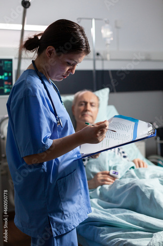 Принти на полотні Medical nurse in scrubs taking notest on cliboard after consultation of sick unwell senior man