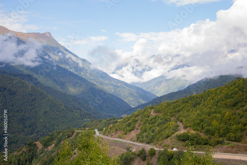 Summer mountain landscape in the Caucasus mountains. Mountain road. Green Forest. Blue sky with clouds covering the peaks of the mountains. A tourist route.