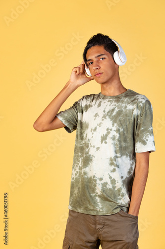 Portrait of young handsome boy, student in casual clothes listening to music isolated on yellow studio backgroud. Human emotions concept. © master1305