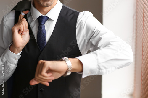 Young man in stylish suit looking at wristwatch, closeup