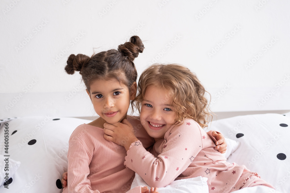 two beautiful diverse kids girls in pajamas hugging on bed in modern bright apartment Stock Photo Adobe Stock