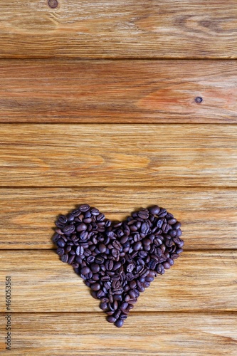 Heap of roasted coffee beans in the shape of a heart on a wooden background