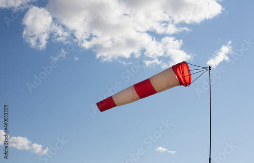 White and red wind flag (windsock) with blue sky background. Air sleeve on a sunny day indicating direction of wind. Windy weather concept. photo