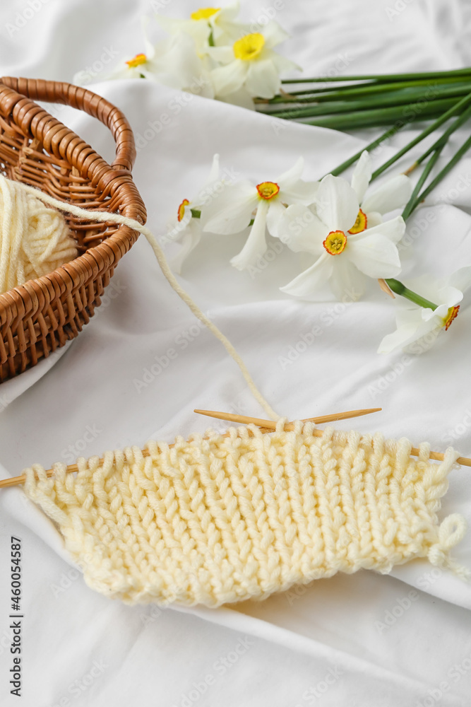 Composition with knitting yarn, needles and flowers on light fabric background, closeup