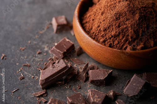 Cocoa powder in bowl and pieces of dark chocolate on a dark grey counter