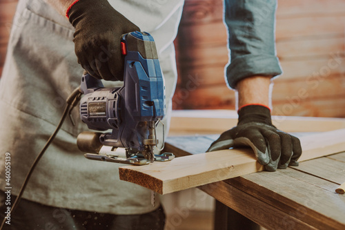 Close up of worker using electric jigsaw in the workshop