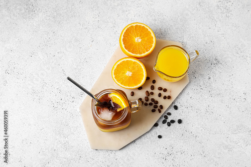 Mason jar of tasty coffee with orange juice and ingredients on light background