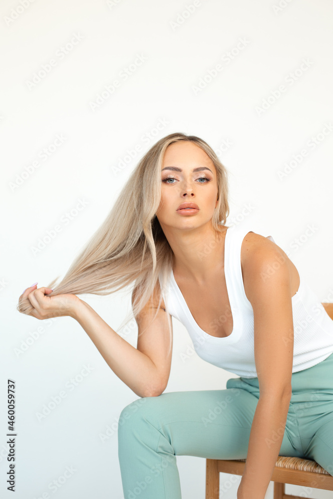 photo of young blonde girl in mint green pantsuit sitting on chair in studio on white background. photo of young blonde girl in mint green pantsuit sitting on chair in studio on white background.
