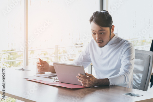 Asian businessman who sitting work by tablet in feeling happy at the office with daylight from window and blur garden background.