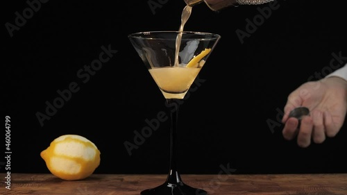 Bartender pouring a dry martini with a lemon twist into a martini glass. Restaurant, nightclub, nightlife concept. 
