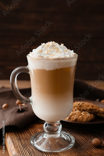 Glass cup of tasty latte with nuts on wooden background