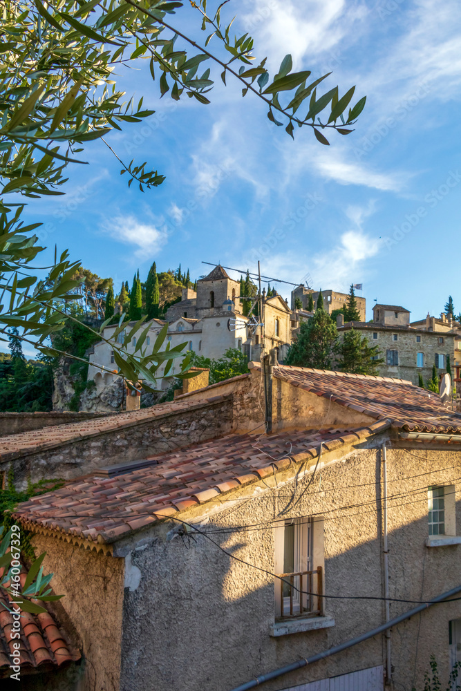 Fototapeta premium Vaison-la-Romaine street view on medieval upper village with red roofs, green trees and blue sky, Provence, France