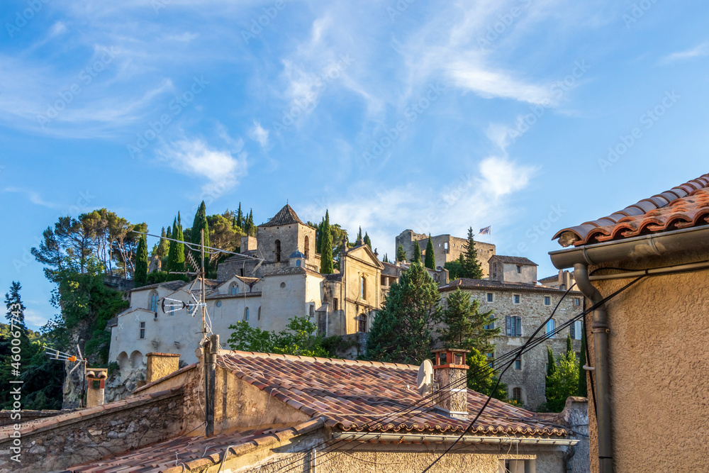 Vaison-la-Romaine street view on medieval upper village with red roofs, green trees and blue sky, Provence, France
