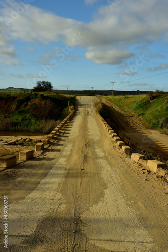 A low water bridge over a dry river bed and a gravel country road disappearing in the distance