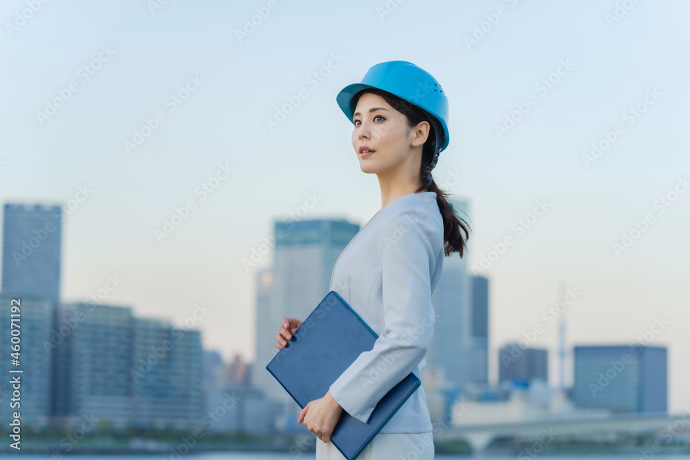 ヘルメットをかぶって都市を眺める女性 設計士 建築家 ヘルメットをかぶって都市を眺める女性 設計士 建築家