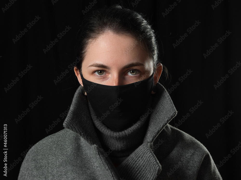 brunette girl in a black COVID mask on a black background brunette girl in a black COVID mask on a black background