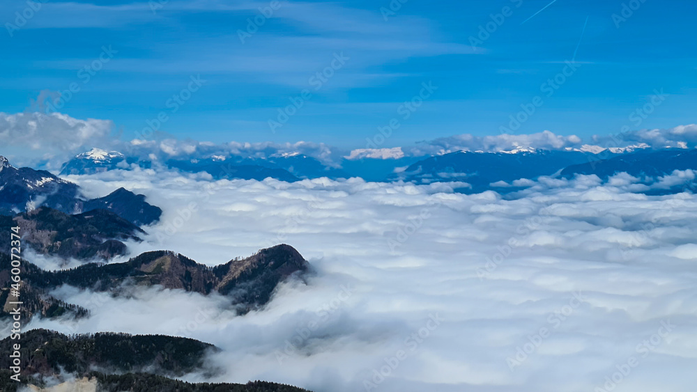 A panoramic view from the top of Alpine peak in Austria. The whole area is shrouded in thick clouds. A few peaks popping out from the clouds. High mountain chains in the back. Carpet from the clouds
