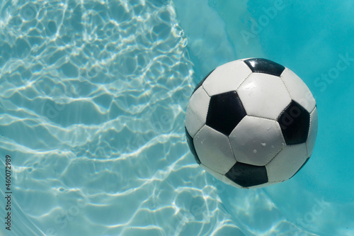 Black and white soccer football floating in a blue clear swimming pool. Summer sport background © ink drop