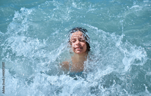 Summer vacation concept. Happy child at sea. Young girl is covered by wave, smiles, rejoices, bathes, swims, splashes in sea waves