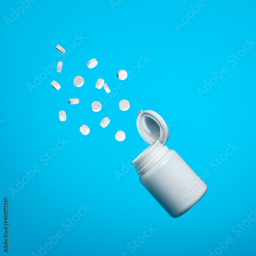 White pills fly out of the jar on a blue background