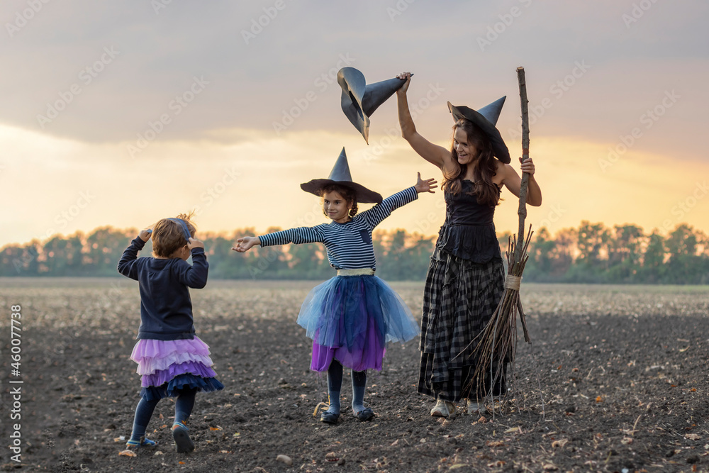 Mother and children in costumes and hats witches play Halloween outdoor. cheerful family of