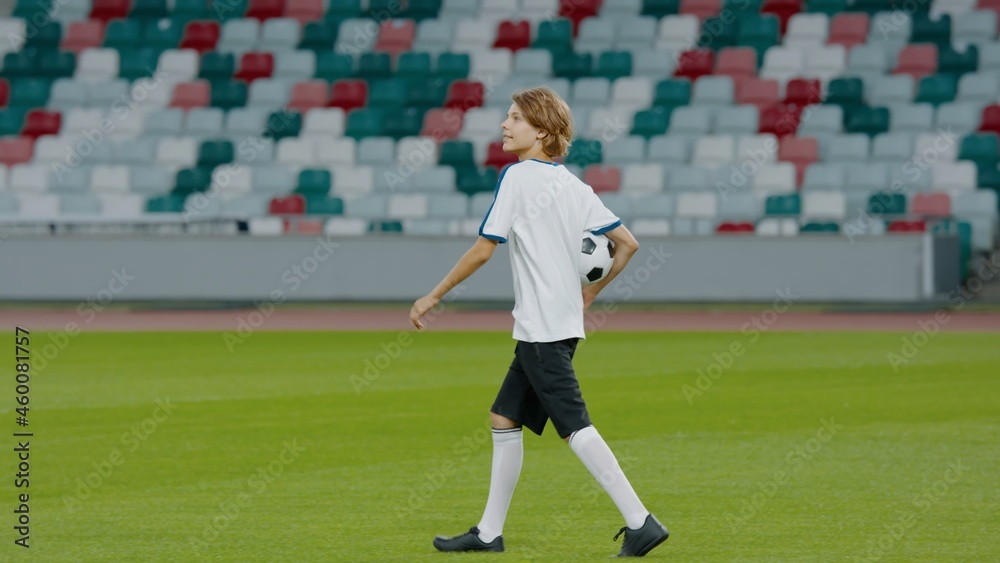 Portarit of Caucasian pre teen kid boy entering the field of huge soccer stadium, holding a ball, dreaming of becoming professional player, soccer star