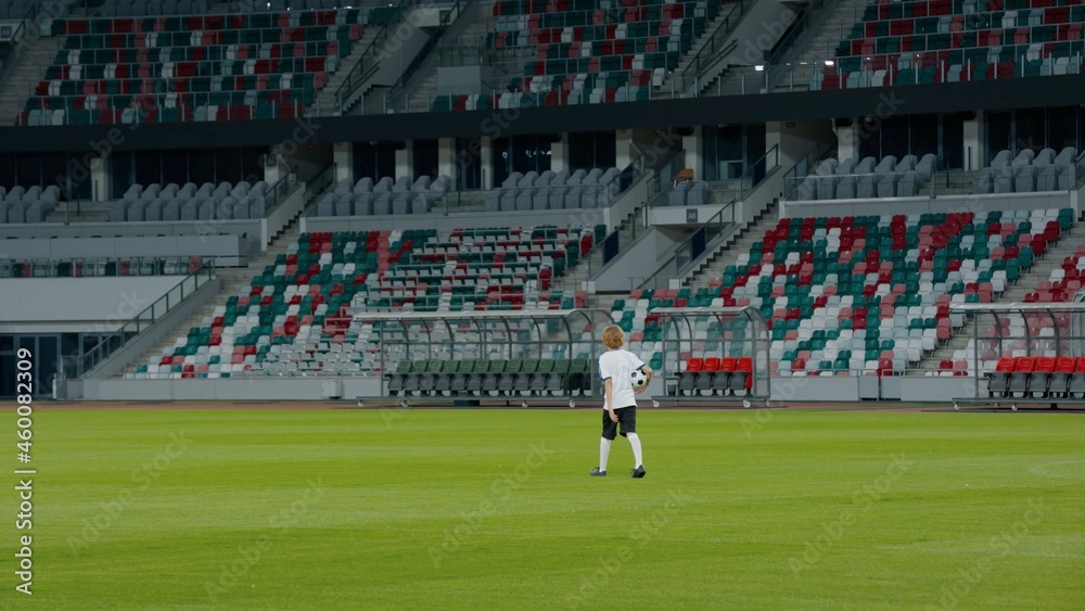Obraz premium WIDE Caucasian pre teen kid boy entering the field of huge soccer stadium, holding a ball, dreaming of becoming professional player, soccer star