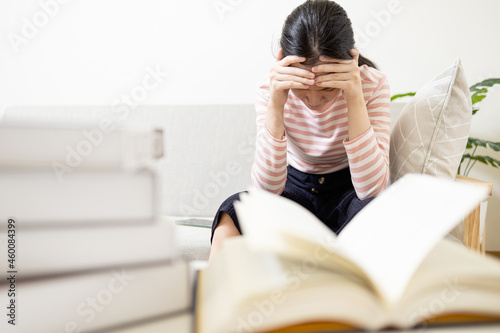 Anxious teenage girl has tension during exam preparation,Stressed worried asian student while studying reading a textbook before final test at her home,afraid of failing the exam,education concept photo