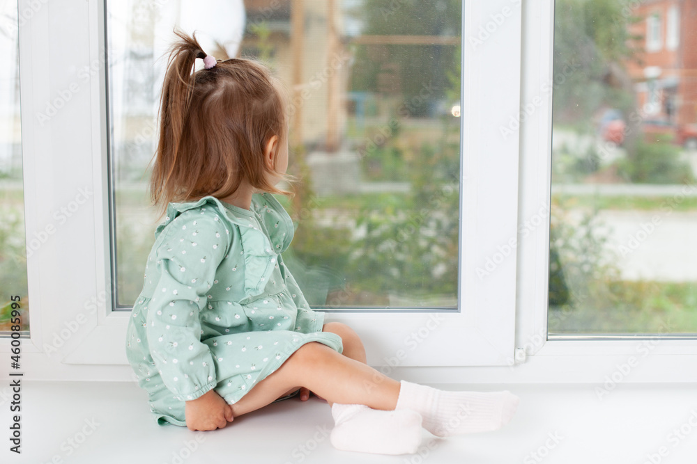 The baby sits on the windowsill of the house and looks at the street. Stroll. Quarantine. The baby sits on the windowsill of the house and looks at the street. Stroll. Quarantine.