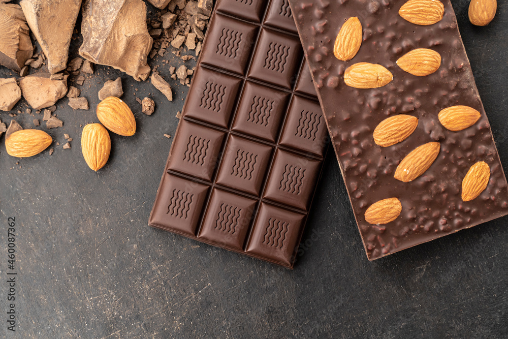 Store Cooking chocolate bars with almonds handmade sweets. Composition of bars and pieces of dark almond chocolate on a black background, top view. Pastry craft on the table Store Cooking chocolate bars with almonds handmade sweets. Composition of bars and pieces of dark almond chocolate on a black background, top view. Pastry craft on the table