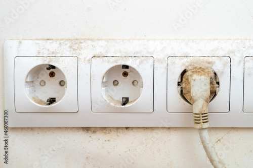 dirty dust on the power socket or connector and electric wire in the room. real old neglected dusty dirt on the electrical computer wire and white wall in the home in the apartment close up photo