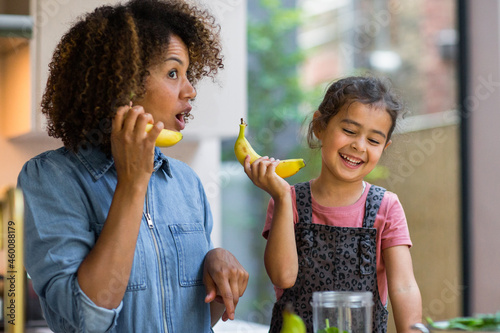 Mixed race girl having fun making a smoothie with mother in kitchen photo