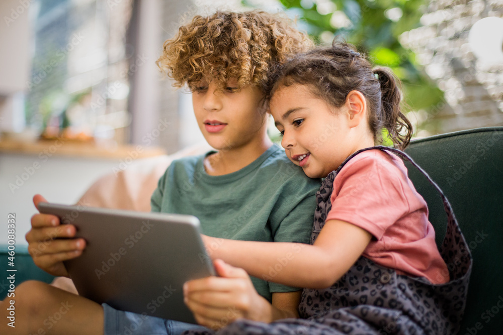 Mixed race girl using digital tablet at home with older brother Mixed race girl using digital tablet at home with older brother