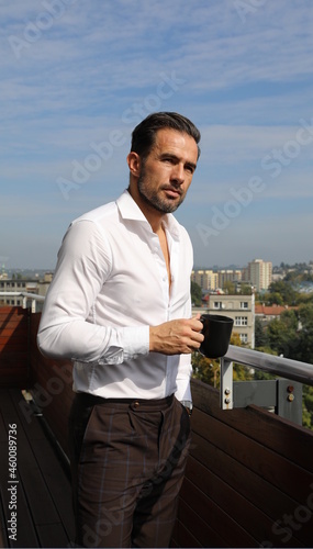 Przystojny brunet w białej koszuli podczas porannej kawy przed wyjściem do pracy.