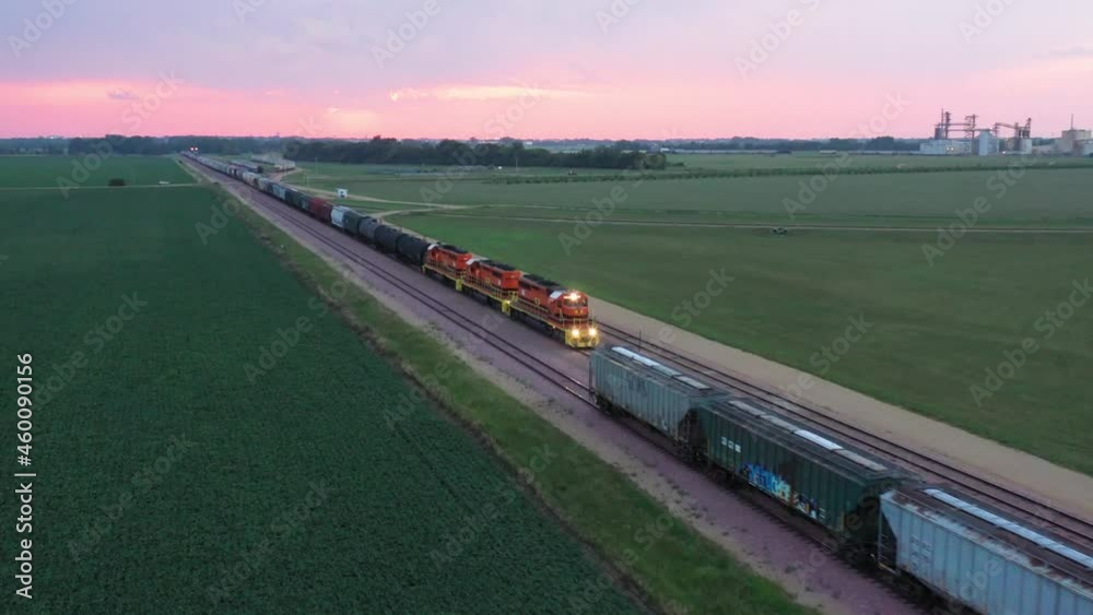 Aerial pull out shot of freight train approaching parked cars in the evening during sunset