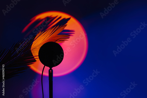 Sunset projector lamp with yellow light and shadow from a palm leaf on dark background.