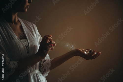woman in a lacy white robe sprays perfume on her wrist
