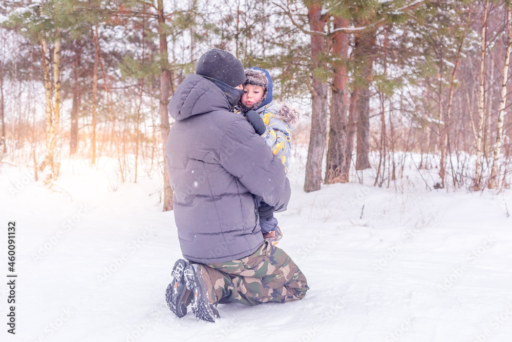 Dad holds and hugs his little son in a snowy forest or winter park. Dad holds and hugs his little son in a snowy forest or winter park.